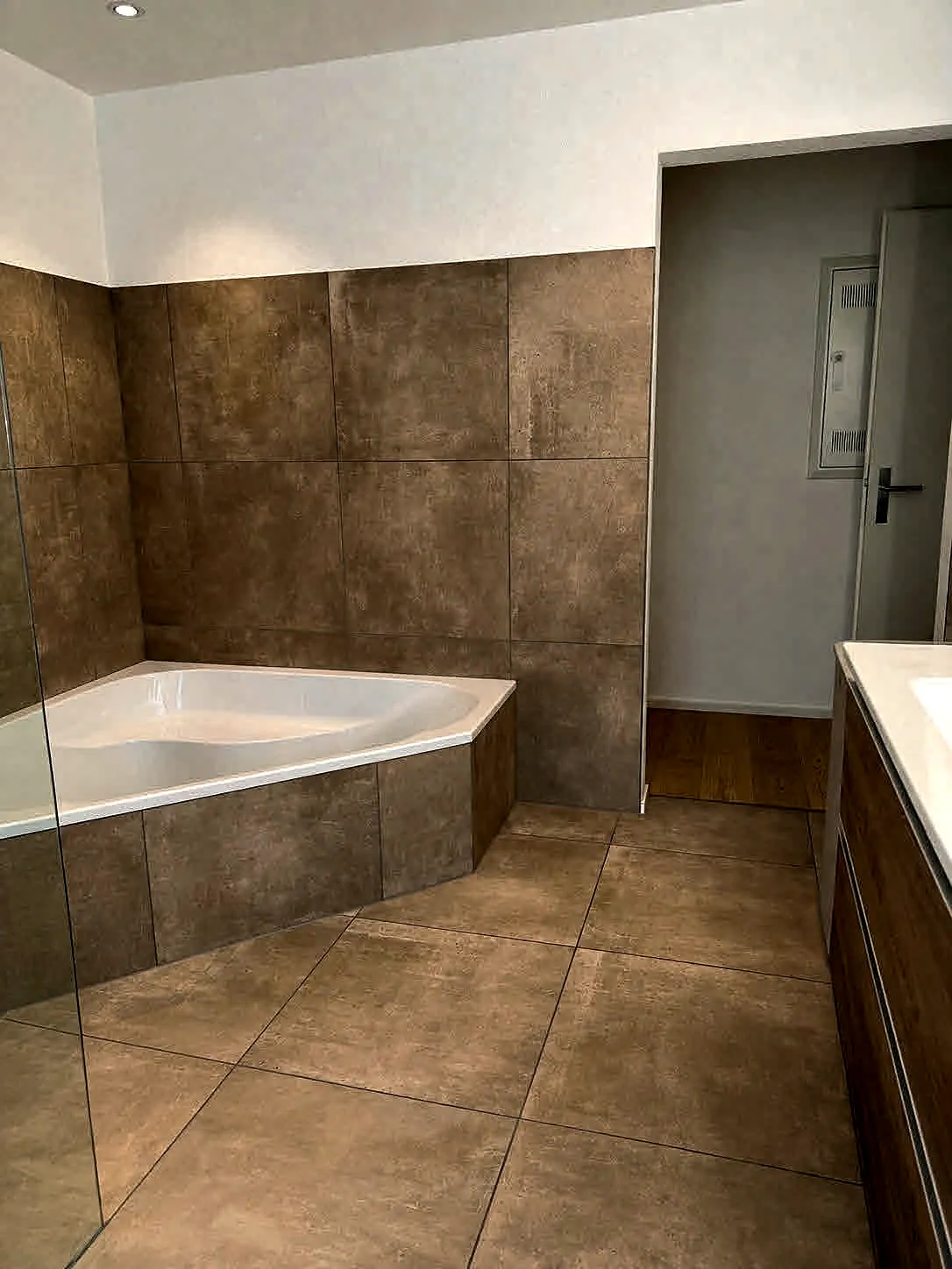 Badezimmer mit Eckbadewanne und grossformatigen Keramikplatten